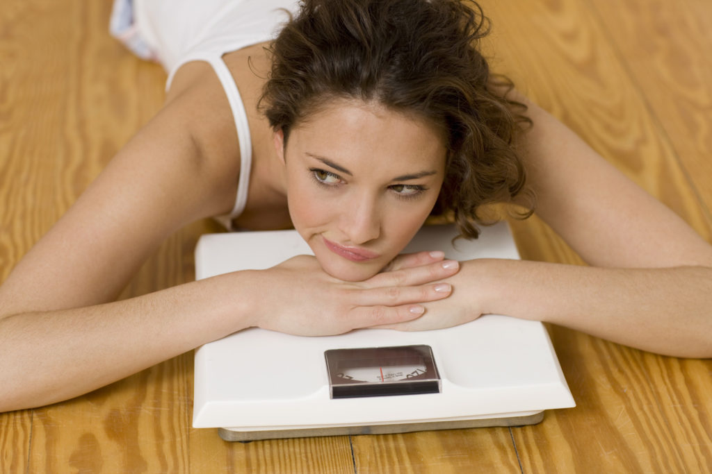 Young woman resting head on scales, musing